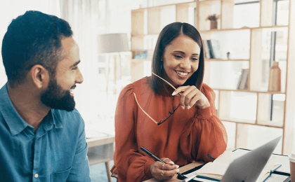 Woman sits next to coworker, looking at computer screen but engaged in conversation